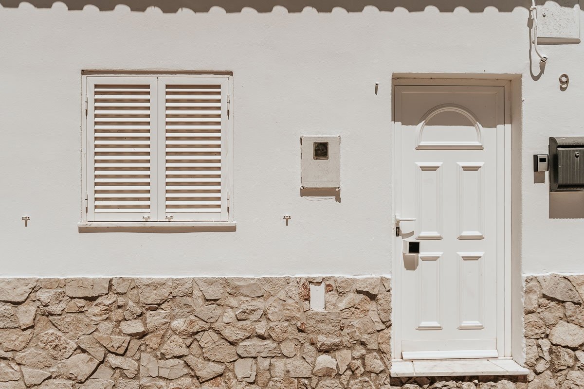 The whitewashed façade of Casa do Vale on a quiet Budens lane, sun on the stone and shutters in soft daylight